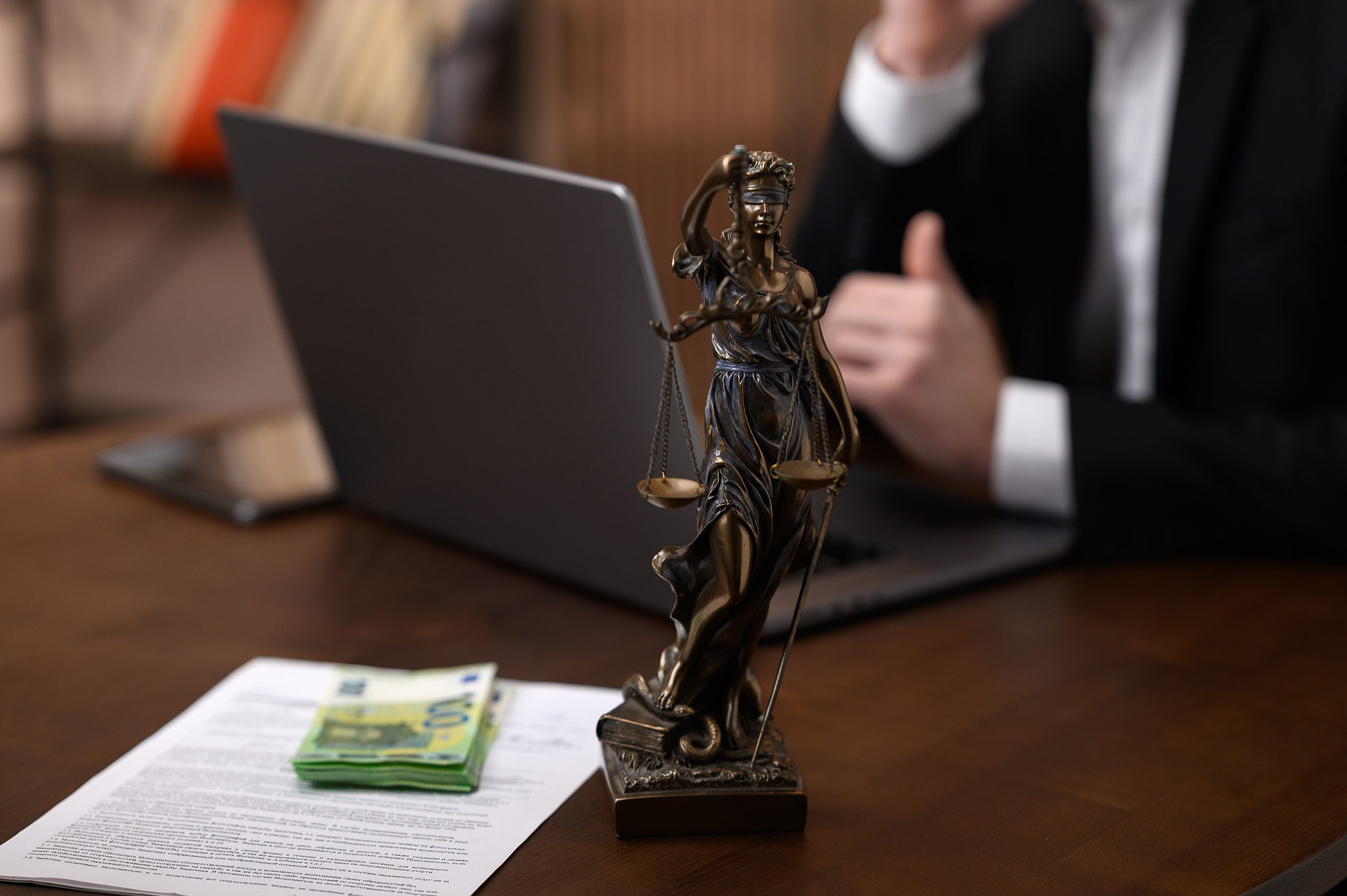Justitia-Statue, Geldnoten und Verträge auf dem Schreibtisch eines Anwalts für Korruptionsstrafrecht.